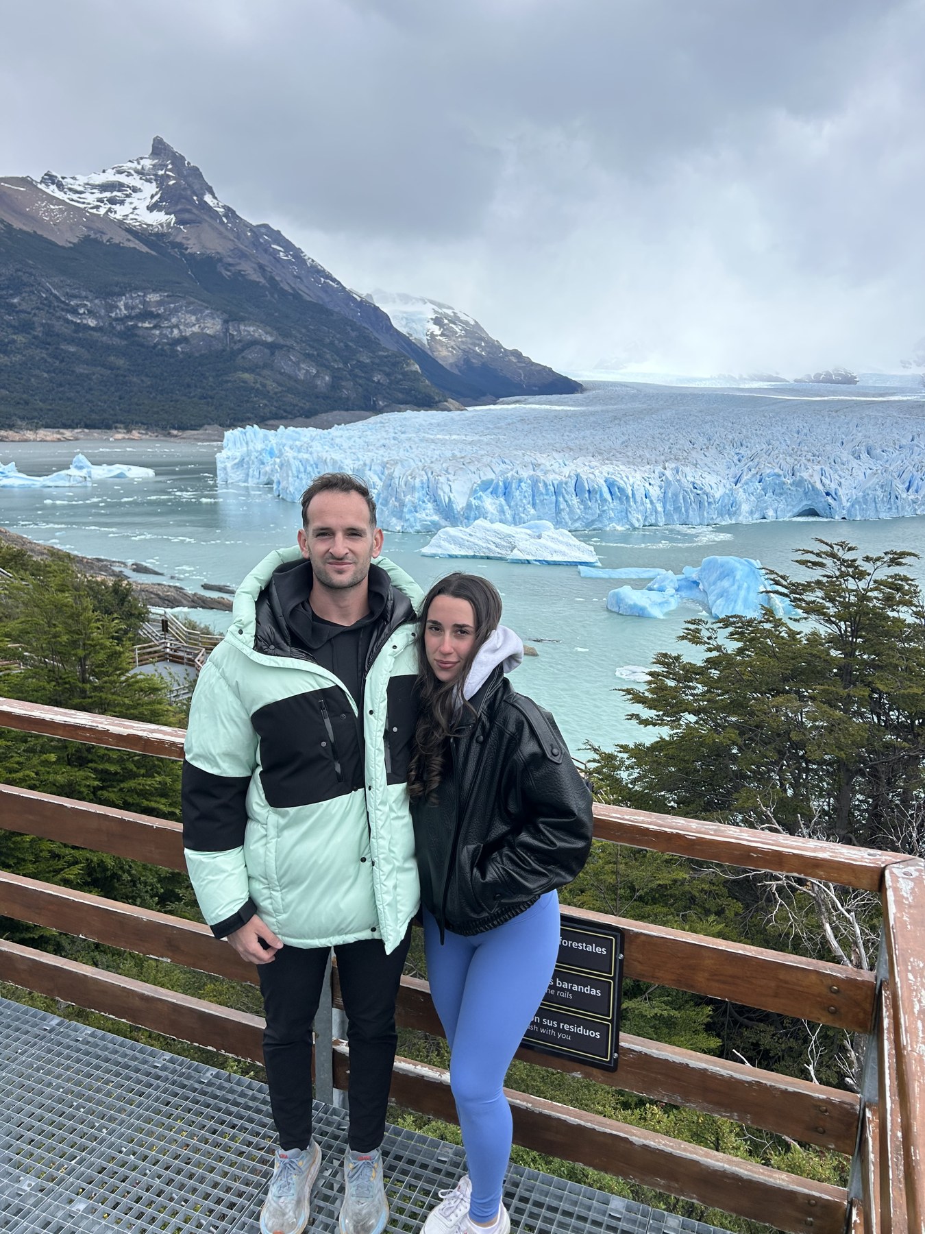 A couple in winter coats on a viewing platform in front of the blue Perito Moreno Glacier, Argentina
