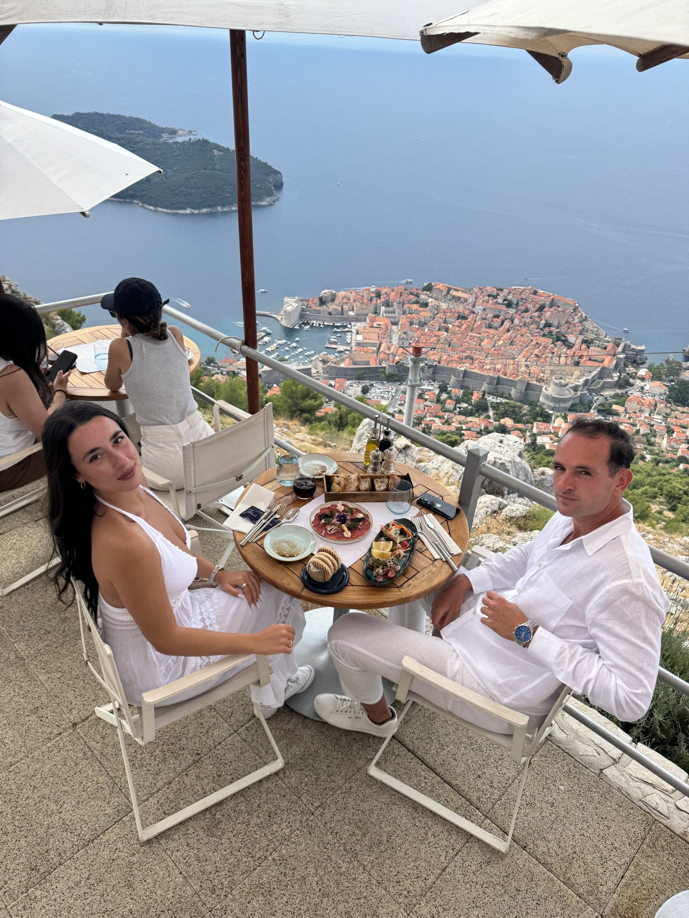 A couple dressed in white at a clifftop restaurant table above the walled old town of Dubrovnik, Croatia