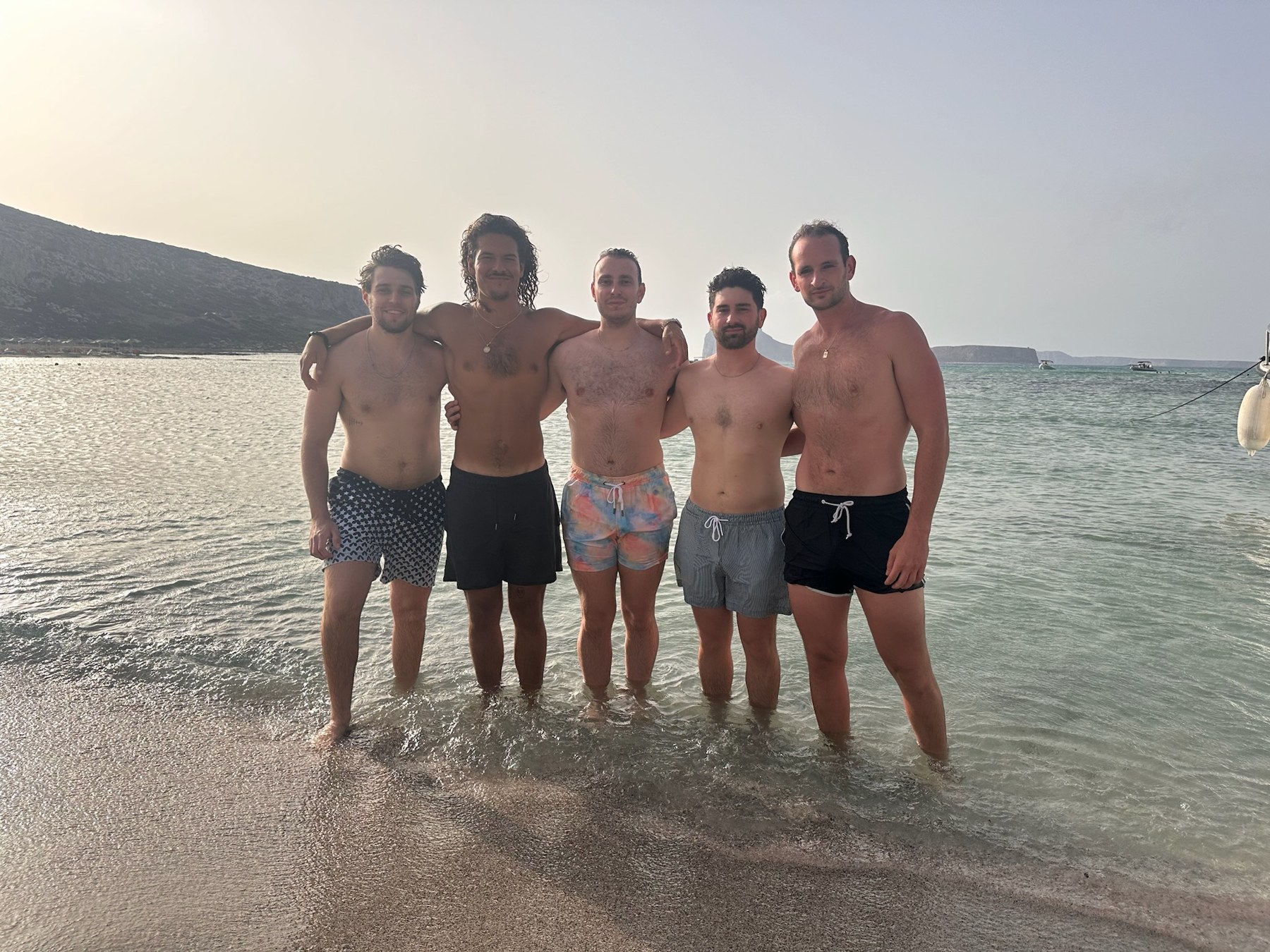 Five men standing in shallow turquoise water at Balos Lagoon, Crete